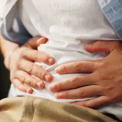 Osoba trzymająca się za brzuch w białej koszulce i niebieskiej koszuli.