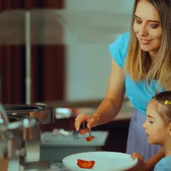 Mama pomaga córce nakładać jedzenie na talerz, stosując zasadę 80/20 diety.