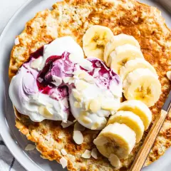 Puszysty omlet bananowy z jogurtem, musem jagodowym i płatkami migdałów na talerzu.
