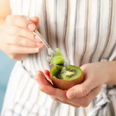 Kobieta trzyma w dłoniach połówkę kiwi i łyżeczkę z kawałkiem owocu.