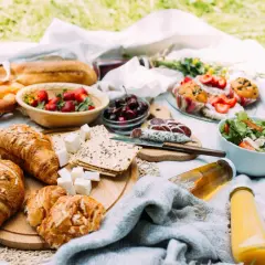 Piknikowy stół z croissantami, owocami, wędliną, sałatką i napojami.