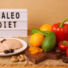 Dieta paleo co to? Na stole surowy kurczak, warzywa, owoce, orzechy i daktyle.
