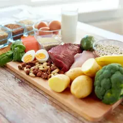 Deska z różnorodnymi produktami spożywczymi: mięso, ryba, jajka, orzechy, warzywa, owoce, mleko i ziarna.