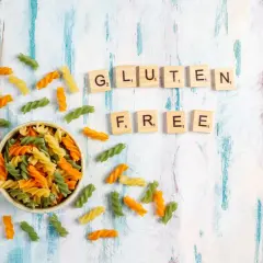 Kolorowy makaron w miseczce i rozsypane po stole, litery układające się w napis "GLUTEN FREE".