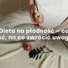 Kobieta w ciąży trzyma jabłko, obok leży drugie jabłko i gałązka.