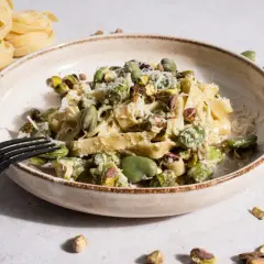 Makaron tagliatelle z bobem i pistacjami, posypany parmezanem, na talerzu.