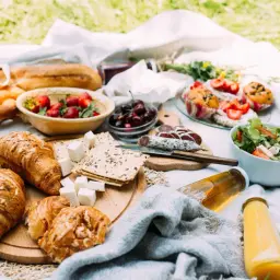 Piknikowy stół z croissantami, owocami, wędliną, sałatką i napojami.