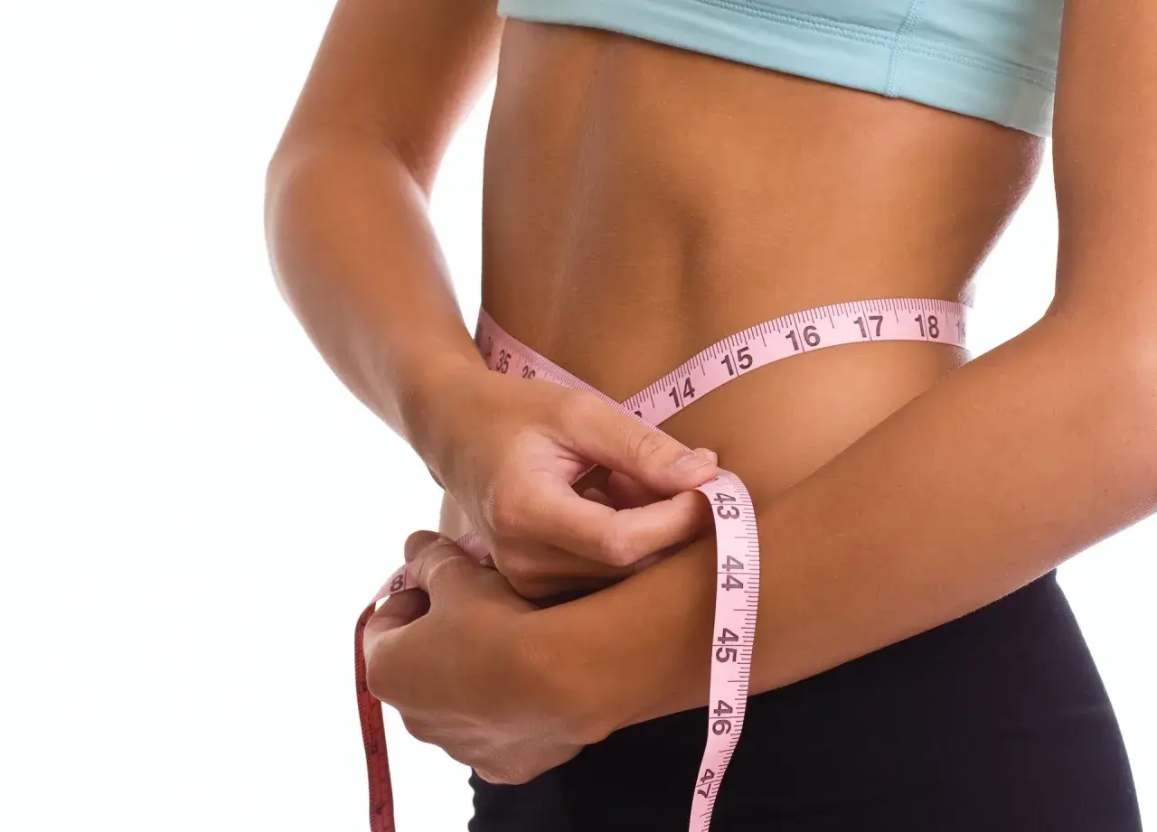 Kobieta mierzy talię centymetrem. Efekty diety 1300 kcal są widoczne.