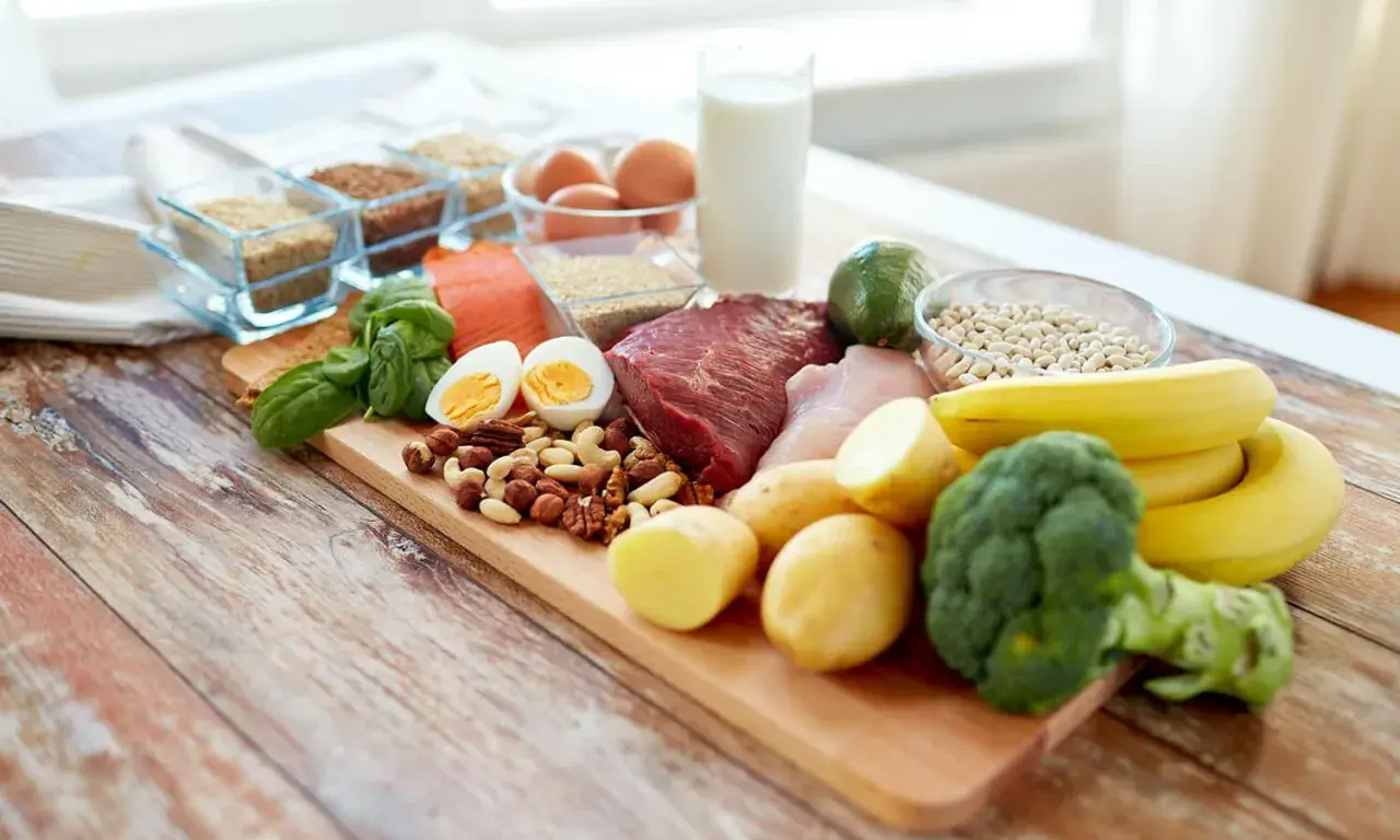 Deska z różnorodnymi produktami spożywczymi: mięso, ryba, jajka, orzechy, warzywa, owoce, mleko i ziarna.
