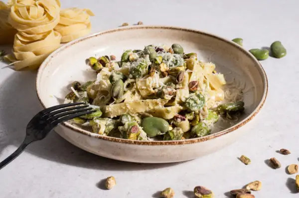 Makaron tagliatelle z bobem i pistacjami, posypany parmezanem, na talerzu.